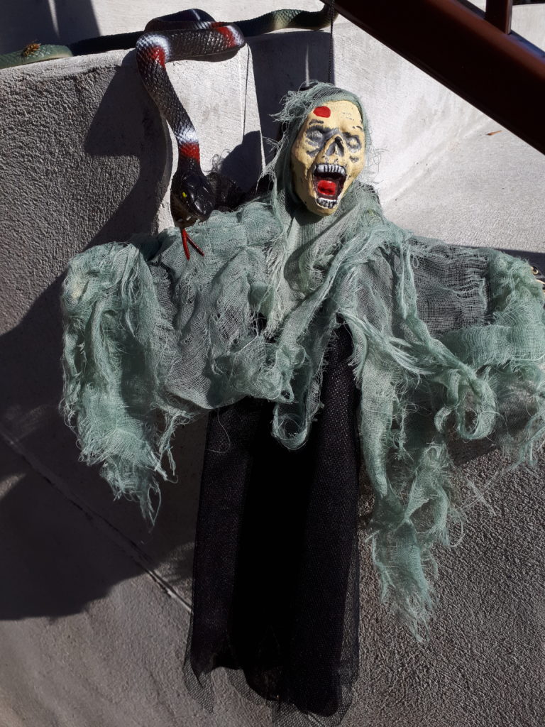 a Halloween ghoul decoration, hanging off the railing of some outdoor steps