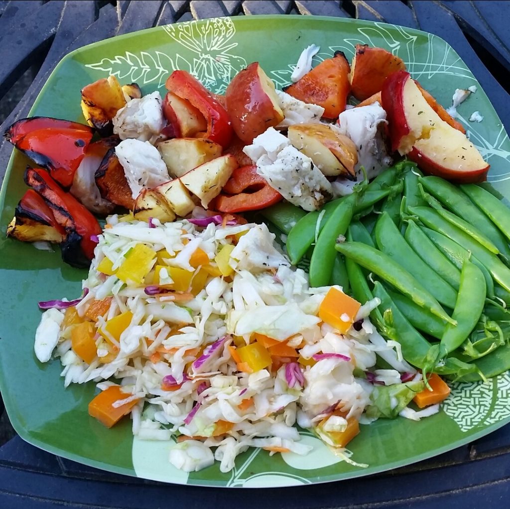 a dinner plate containing a home-made meal; grilled fish and apples, with sides of sugar snap peas and lime coleslaw