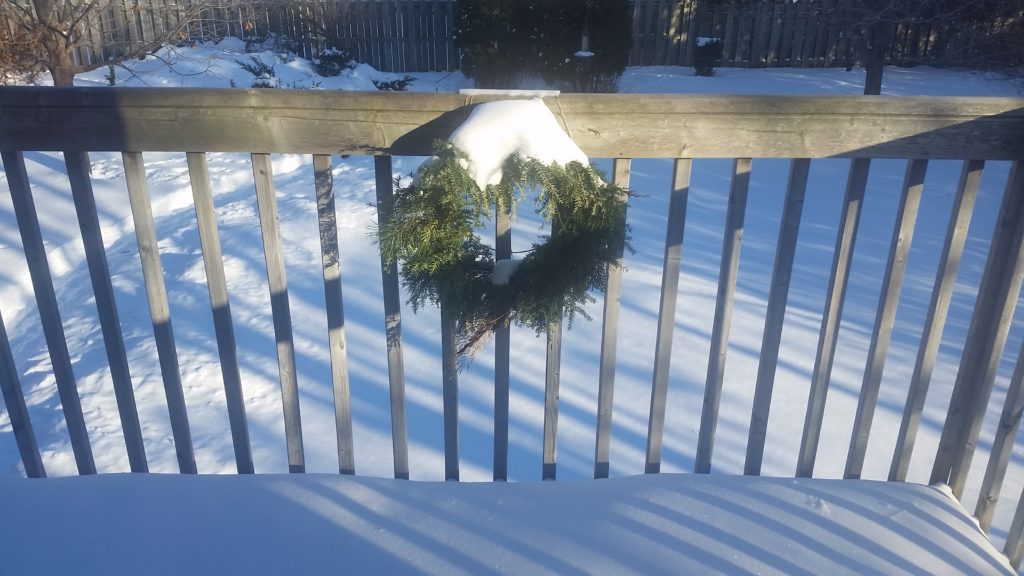 a Christmas wreath on the railing of a balcony, covered in snow