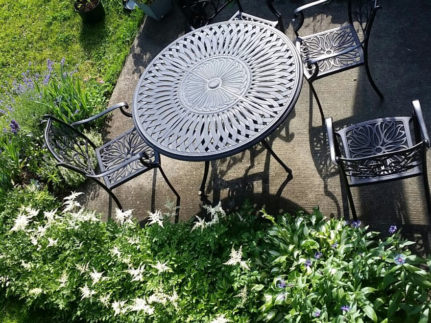 a wrought-iron table and chairs on a patio surrounded by gardens