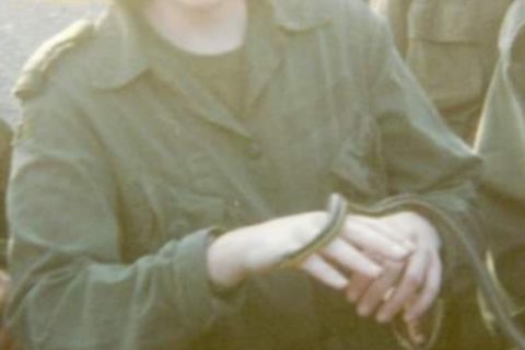 a female military officer wearing combat fatigues, standing with her hands at waist level, letting a small snake holding a small snake move between her two hands