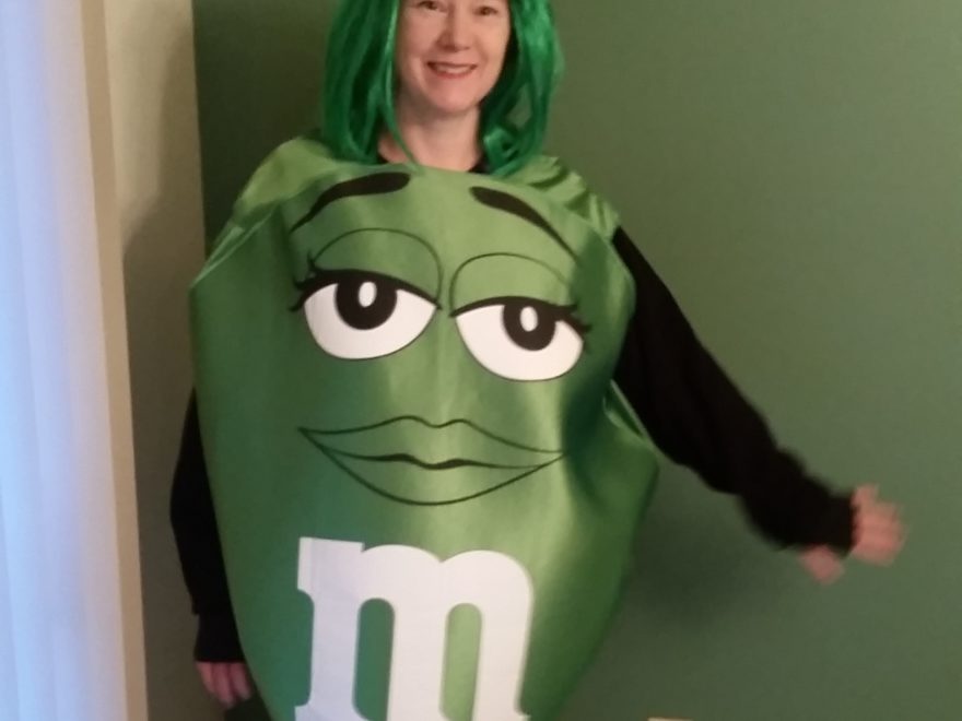 a woman dressed in costume, as a green M&M's candy and wearing a green wig