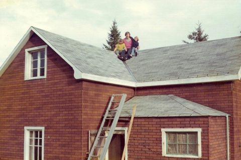 a man and two young girls on the roof ridge of a two-story house