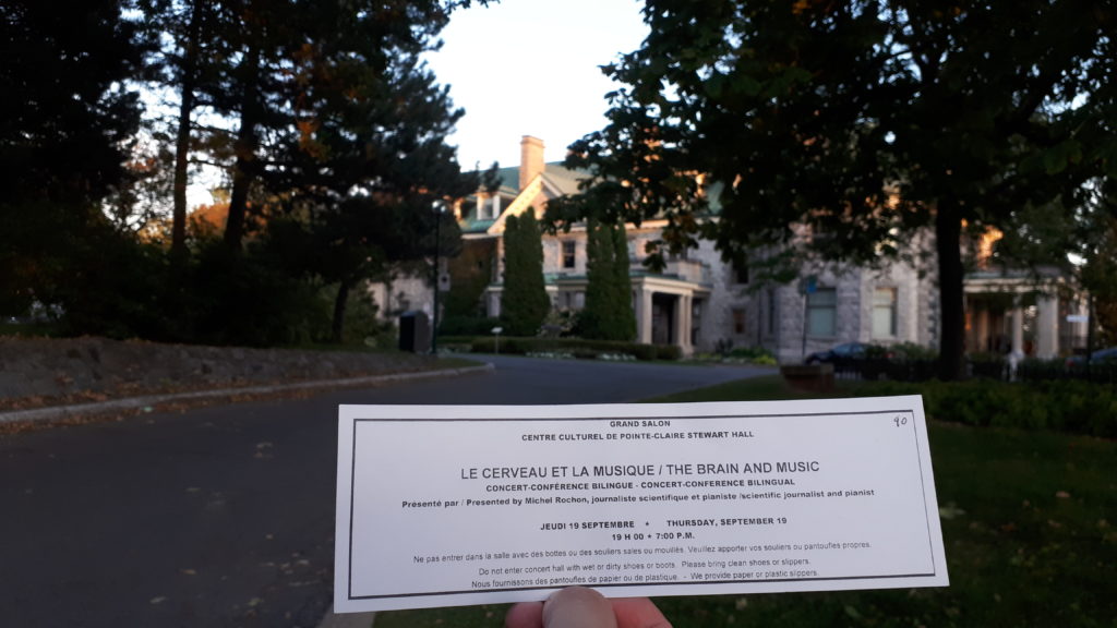 an old stone mansion, now a cultural centre. In the foreground, someone is holding a ticket for an event. The ticket says "The brain and music, a bilingual concert-conference".