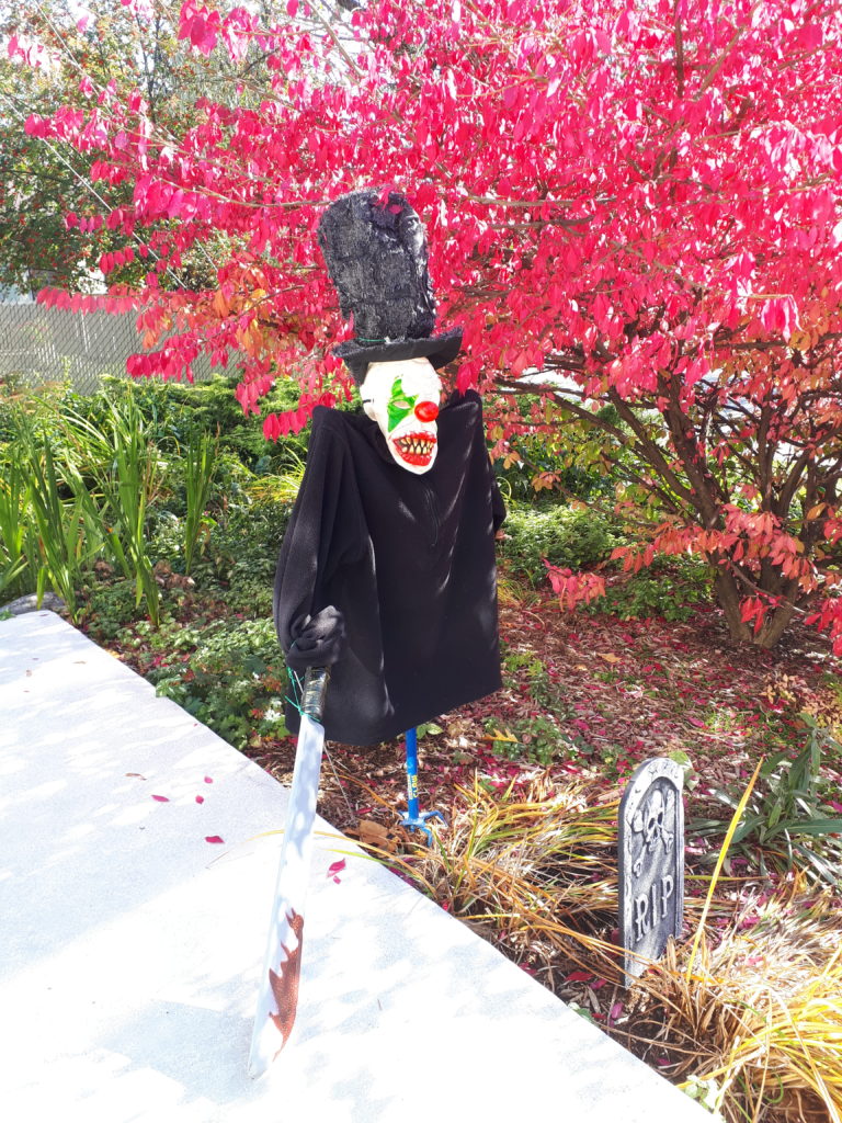 a front yard decorated with a life-size creepy clown and fake tombstones, for Halloween