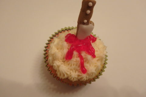 a Halloween cupcake decorated to look like it has been stabbed by a knife and is oozing blood