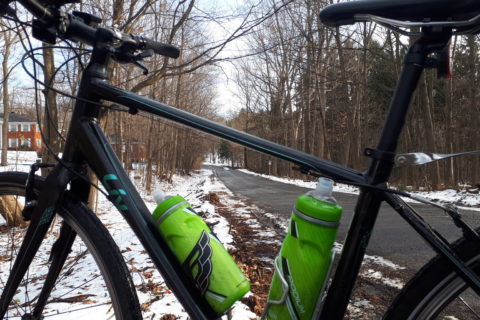 a woman's bicycle, at the bottom of a small hill in a forest. There is snow on the ground, but not on the road which is wet.