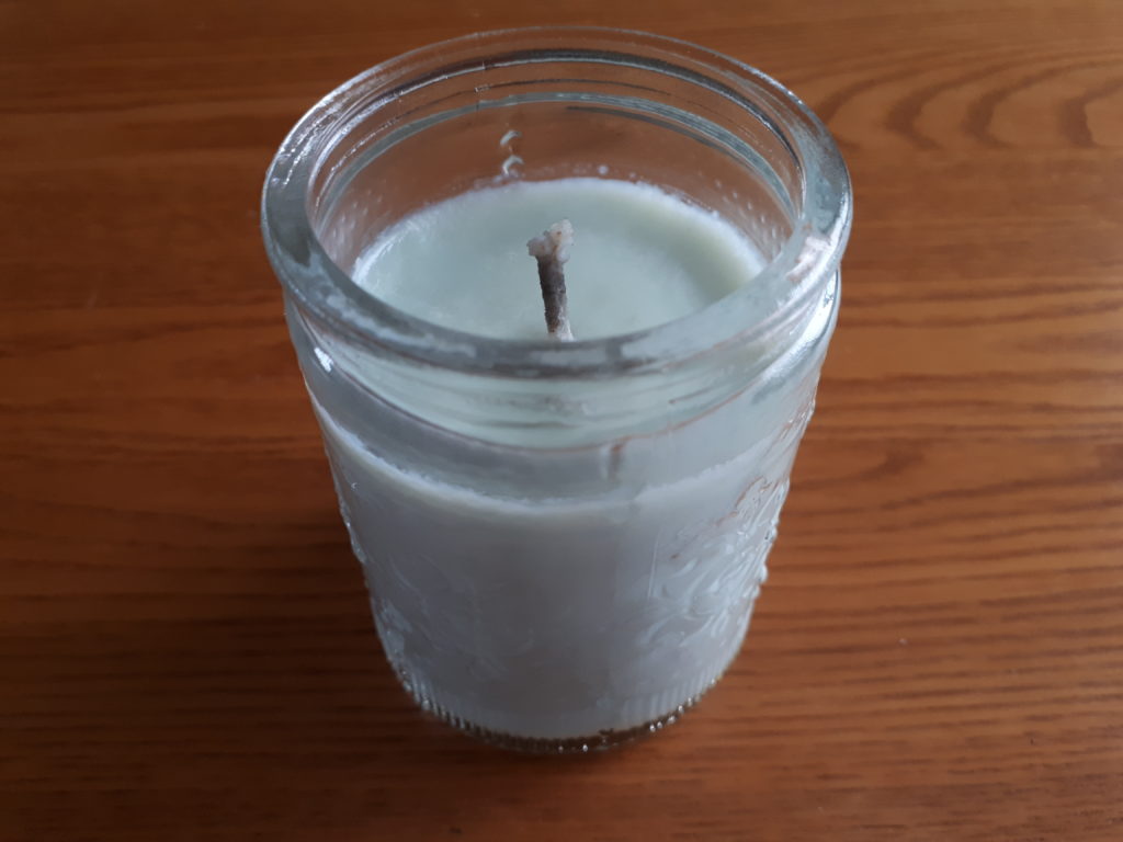 a small soy candle in a glass container, placed on a wood table. The candle is not burning.