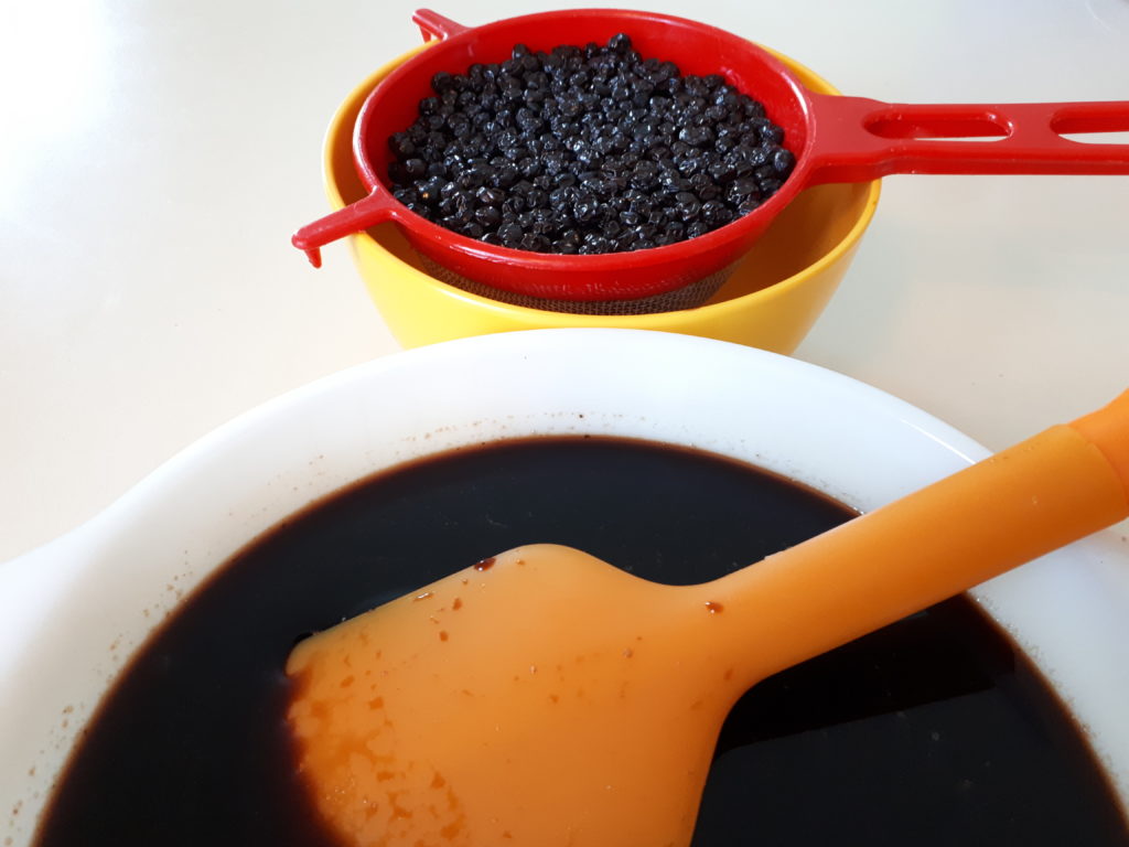 a bowl of cooked elderberries beside a bowl of not-yet-finished elderberry syrup