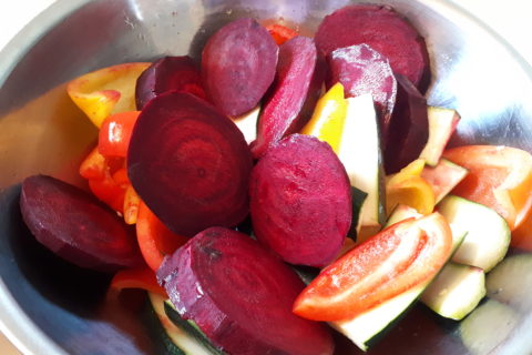 a large metal bowl filled with sliced beets and veggies, brushed with olive oil, ready to be grilled