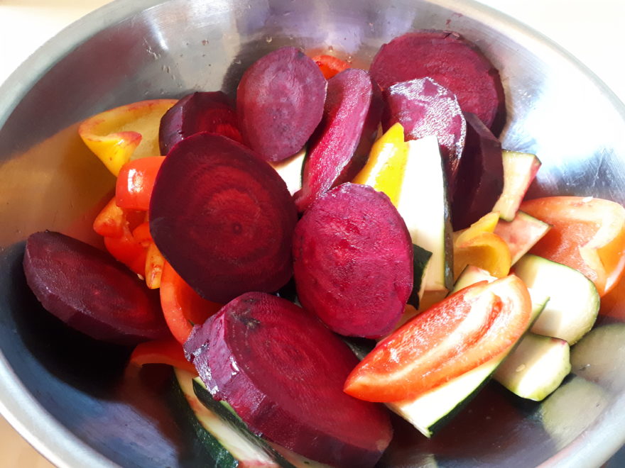 a large metal bowl filled with sliced beets and veggies, brushed with olive oil, ready to be grilled