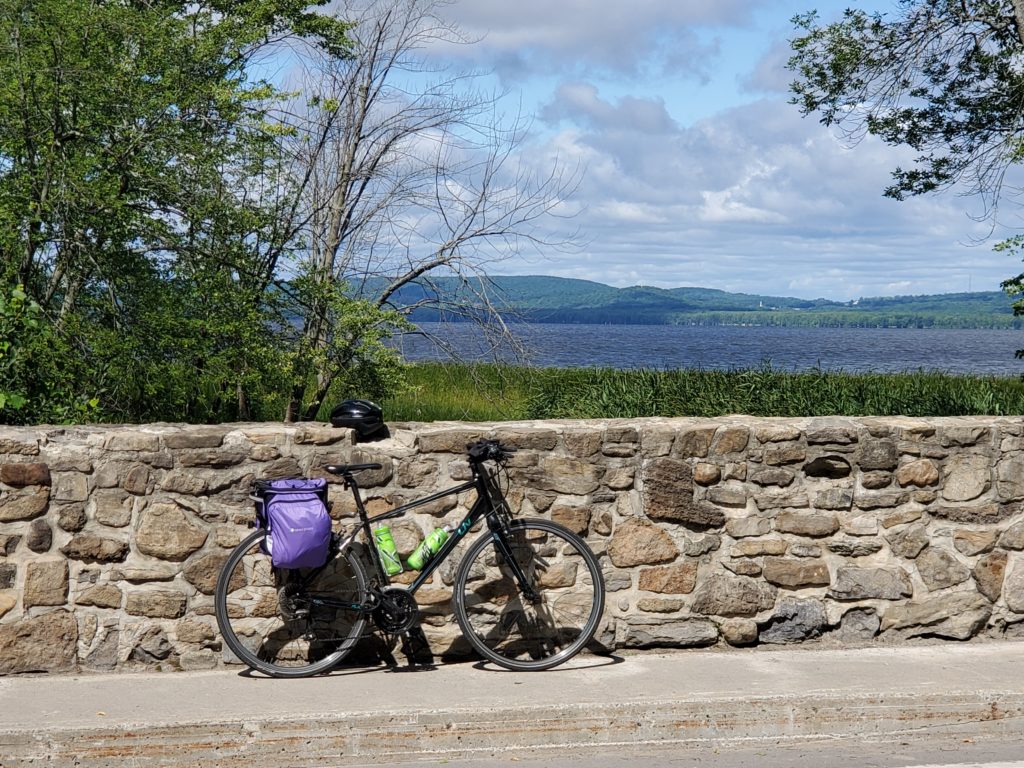 a bicycle leaning against the old stone wall of a bridge, overlooking a lake with low mountains in the background