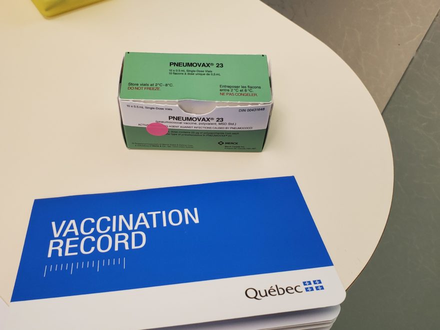 A vaccination record booklet on a table beside a of pneumonia vaccine