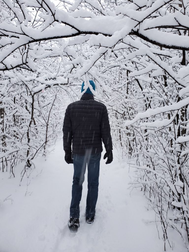 a man walking on a snowy trail through a forest