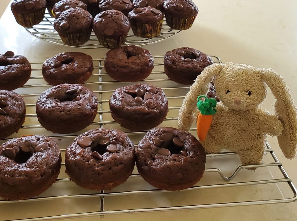 A small plush rabbit toy on a tray of baked chocolate donuts